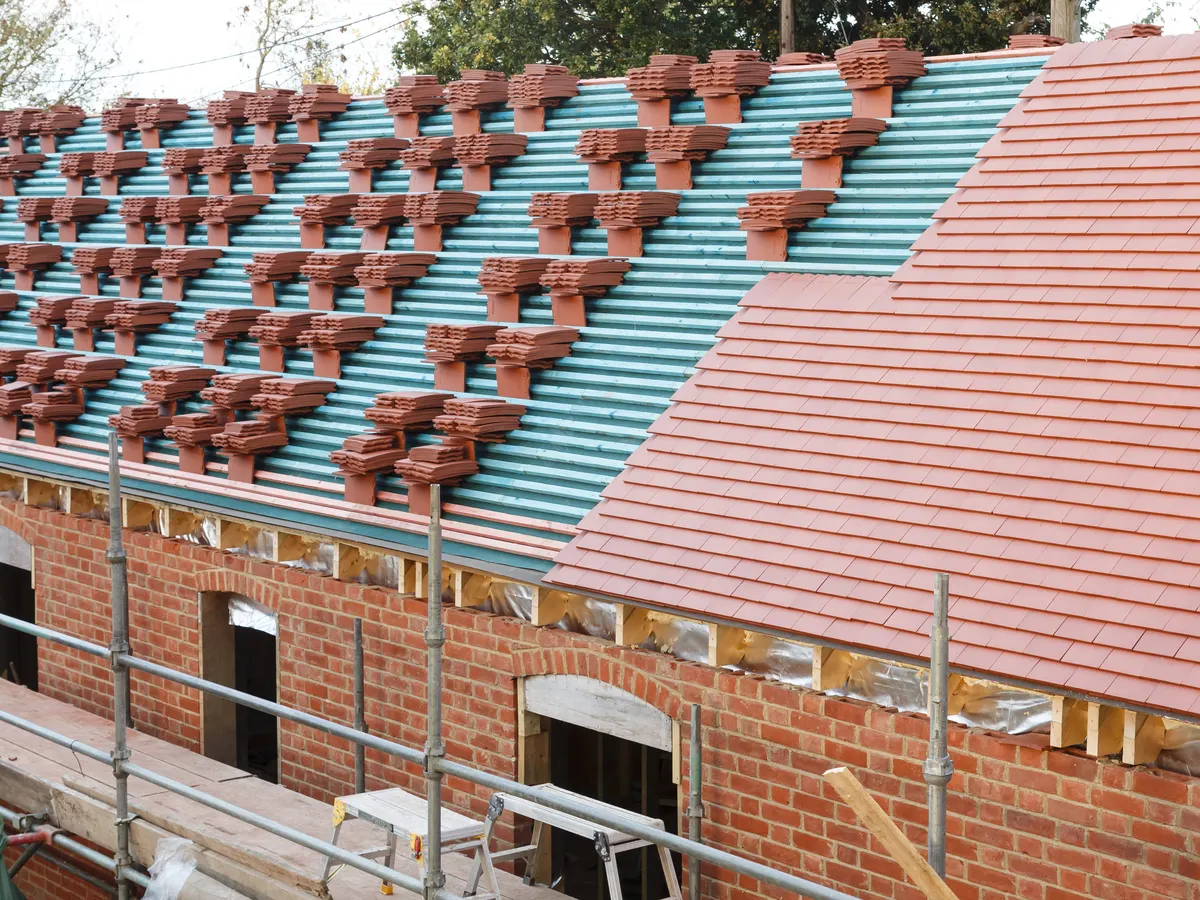 A pitched roof being re-tiled, with new tiles stacked along the battens