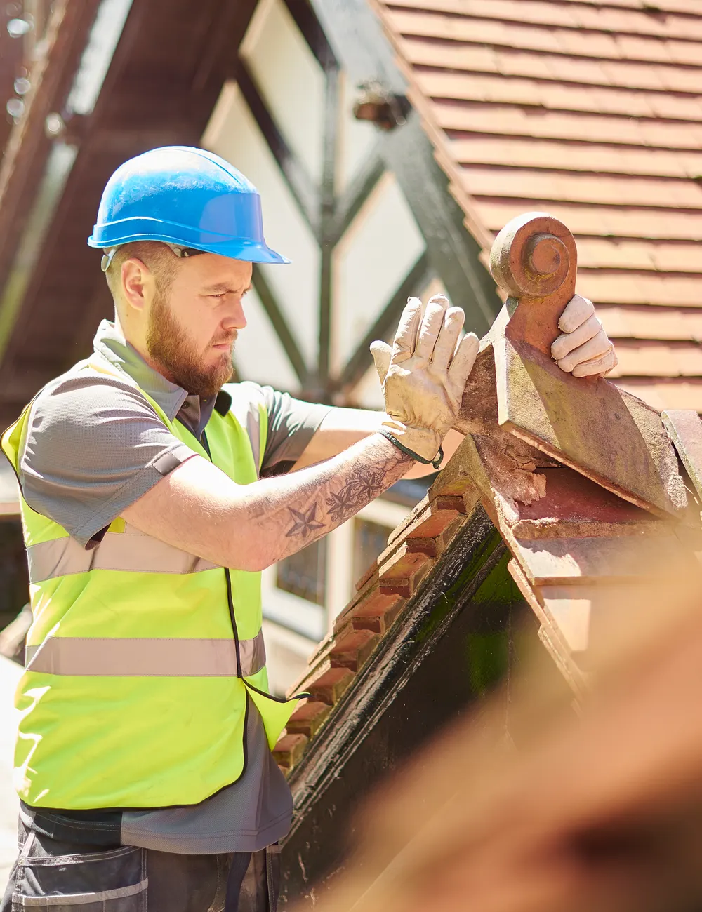 A roofer in a hard hat carrying roof tiles across a scaffold