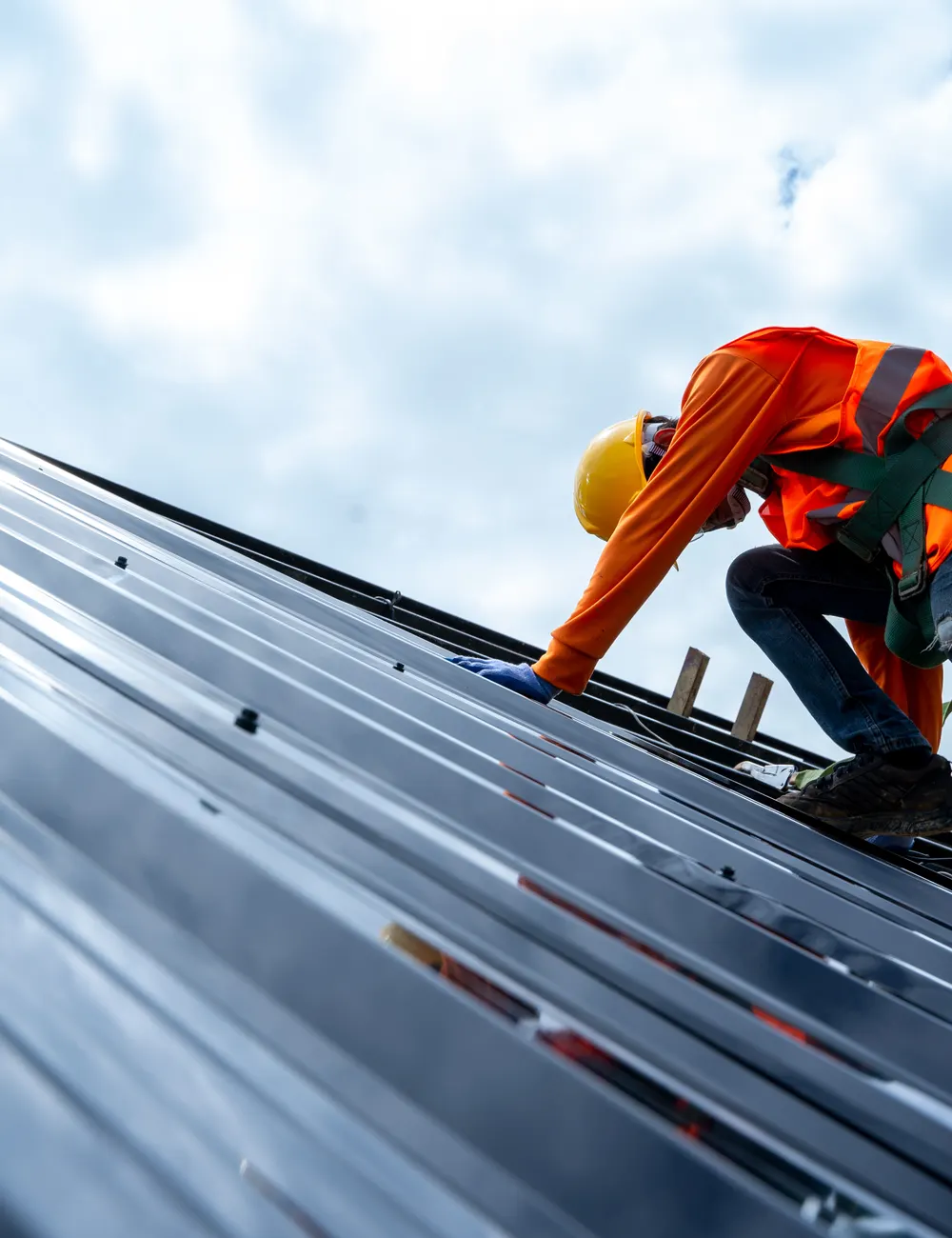 A roofer in a harness working on a metal roof