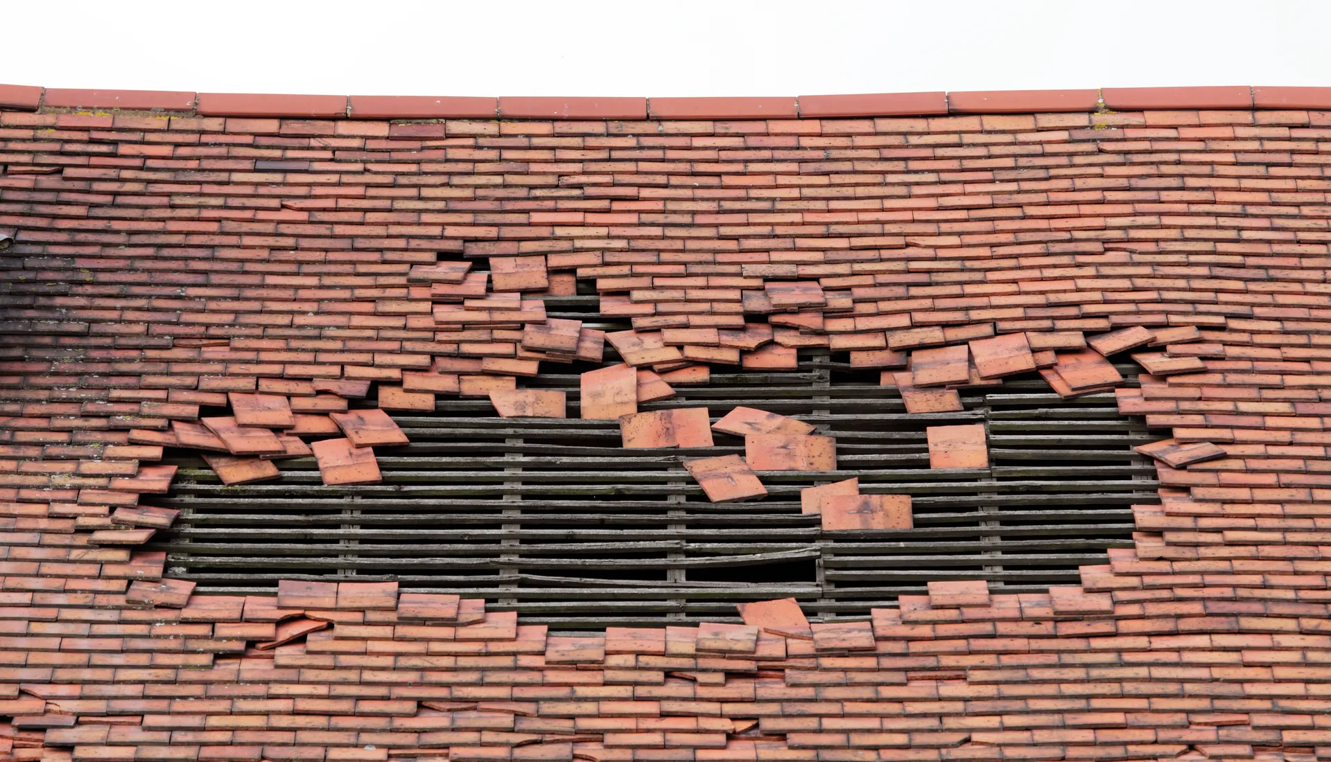 A tiled roof with a large section of tiles blown off