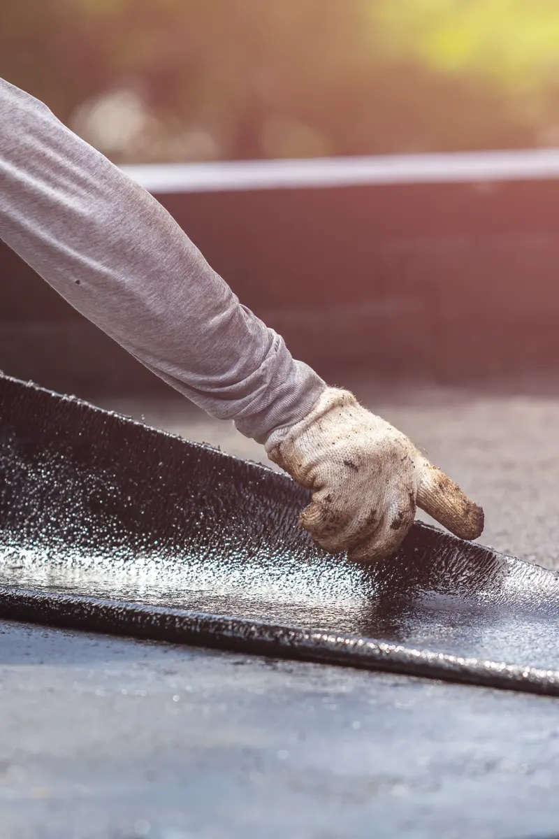 A roofer pressing down a new layer of roofing felt
