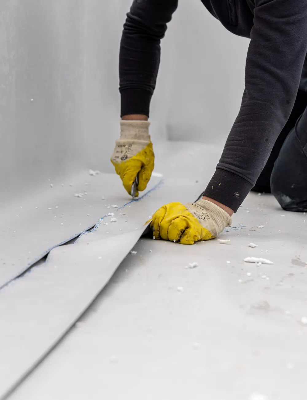 A roofer trimming fibreglass matting on a flat roof