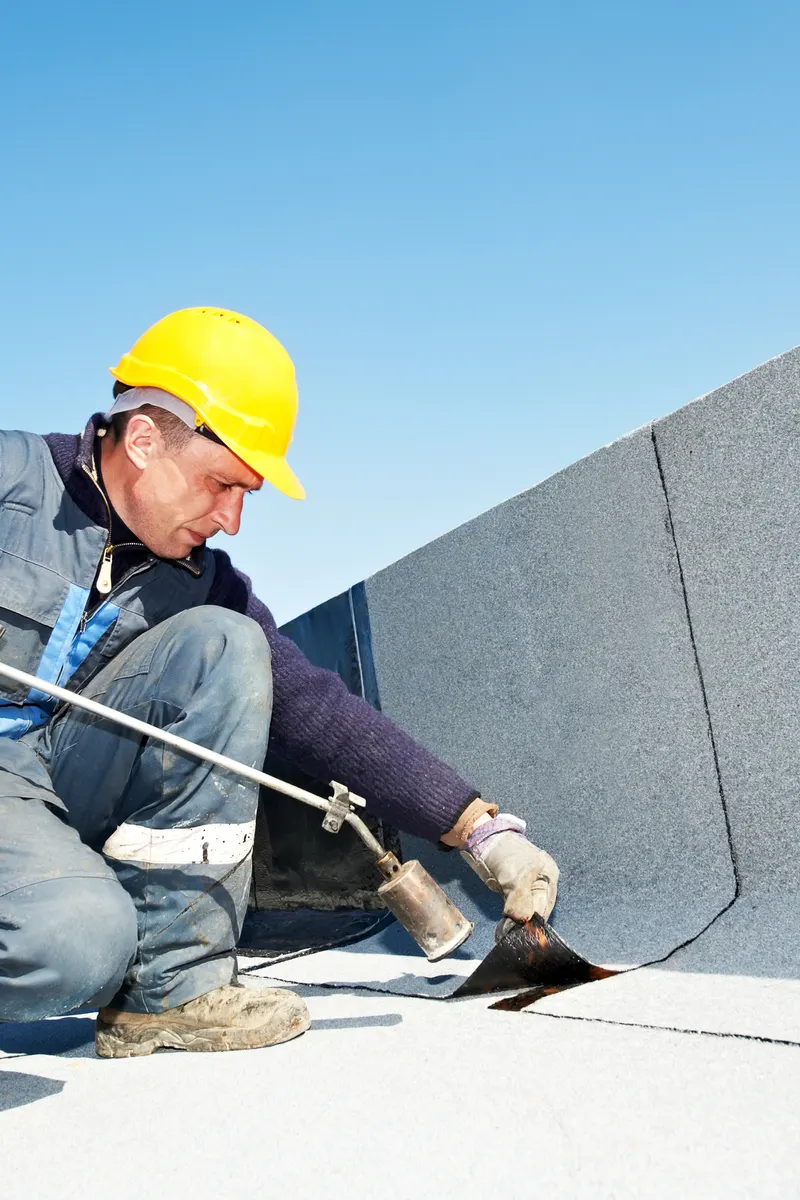 A roofer sealing a flat roof upstand with a gas torch