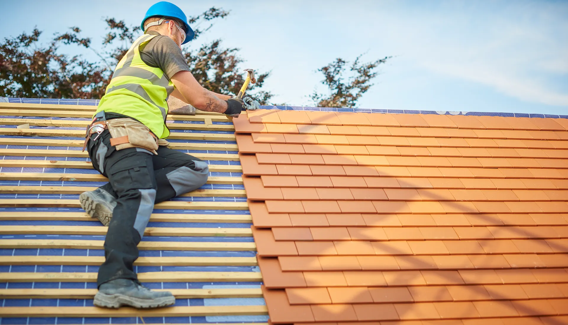 A roofer laying new tiles over fresh battens and underlay