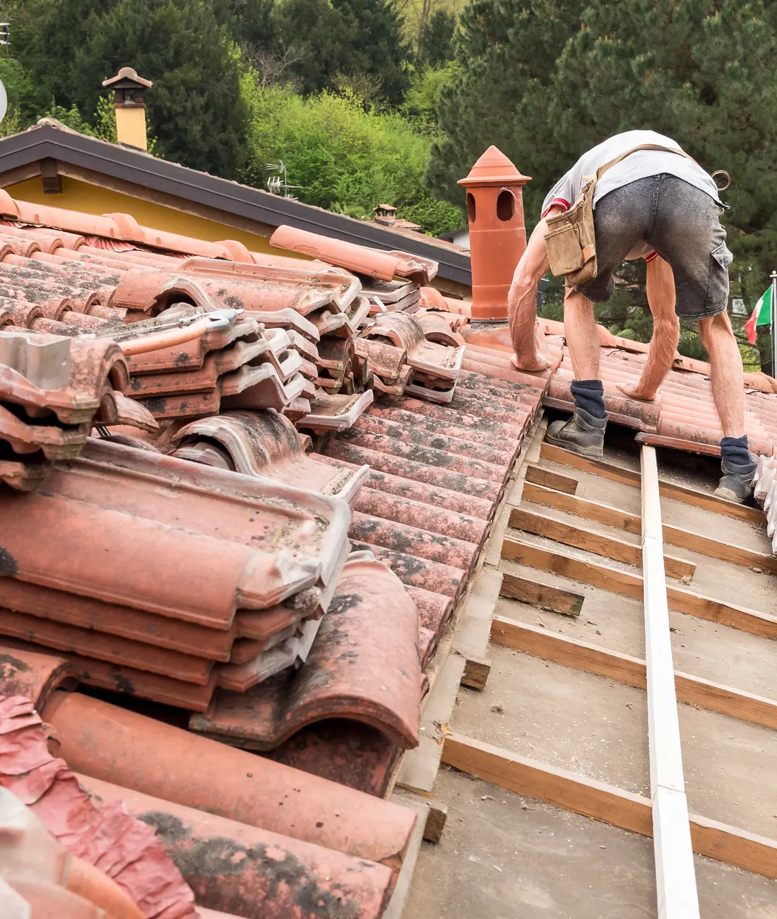 A roofer lifting broken clay tiles to repair a roof