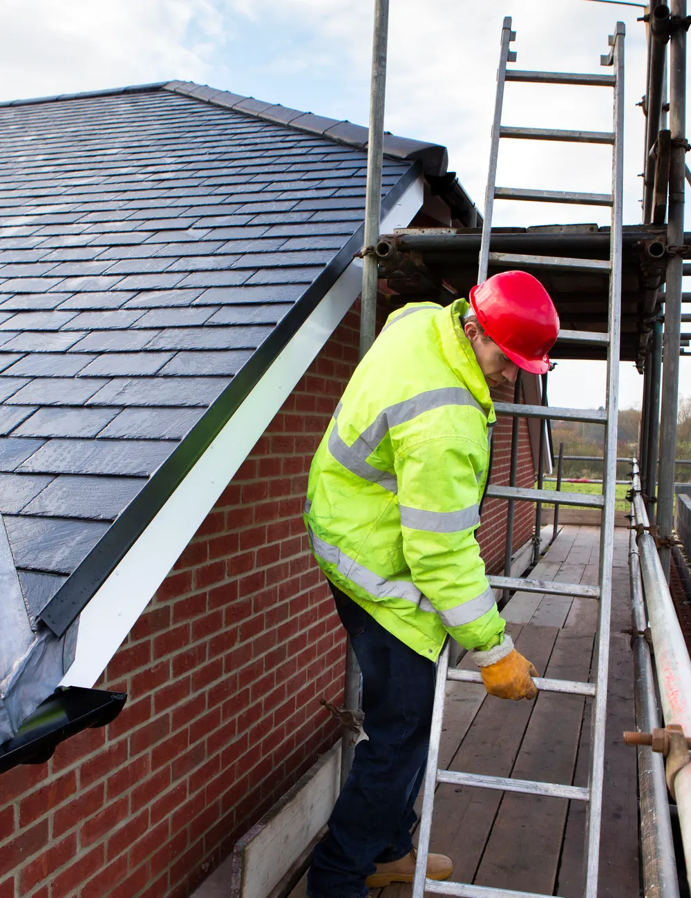 A roofer on a scaffold beside a newly slated roof