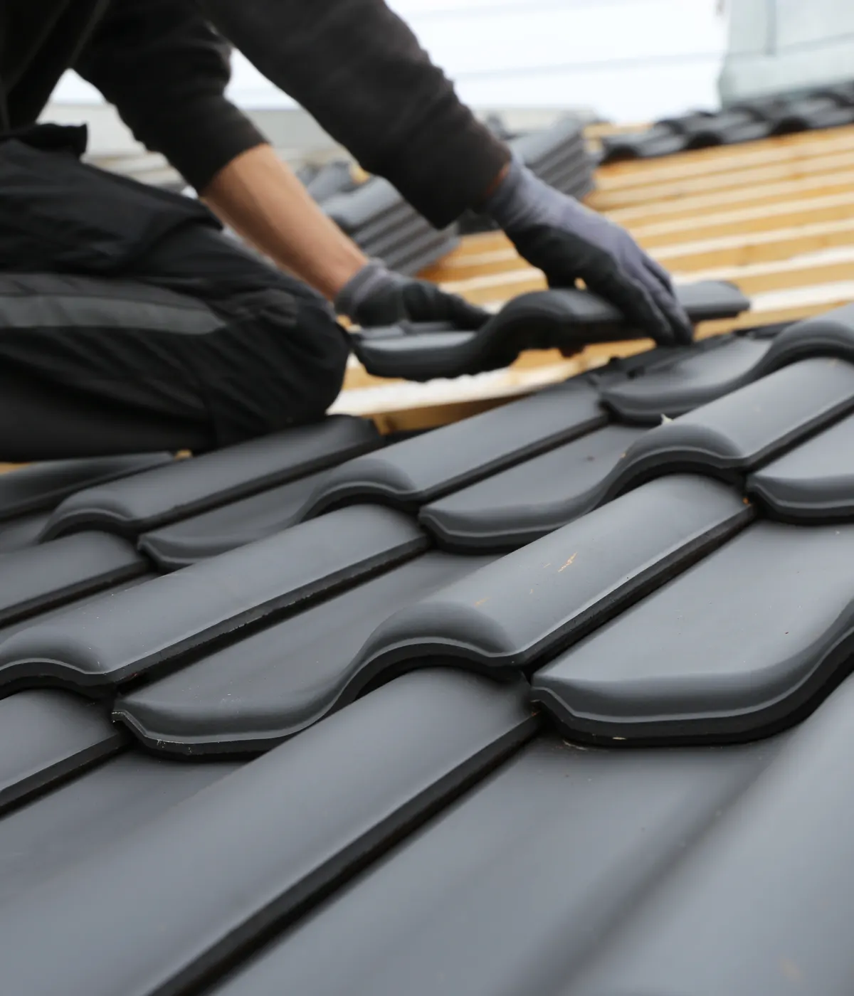 Dark interlocking roof tiles being laid by hand
