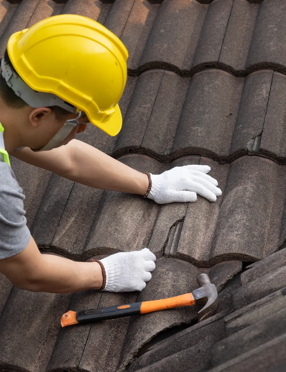 A roofer in a hard hat fixing concrete roof tiles